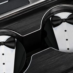 Set of two tuxedo-inspired ceramic car coasters displayed inside luxury vehicle cup holders with elegant black bowtie artwork and modern NicNacBooteek styling.
