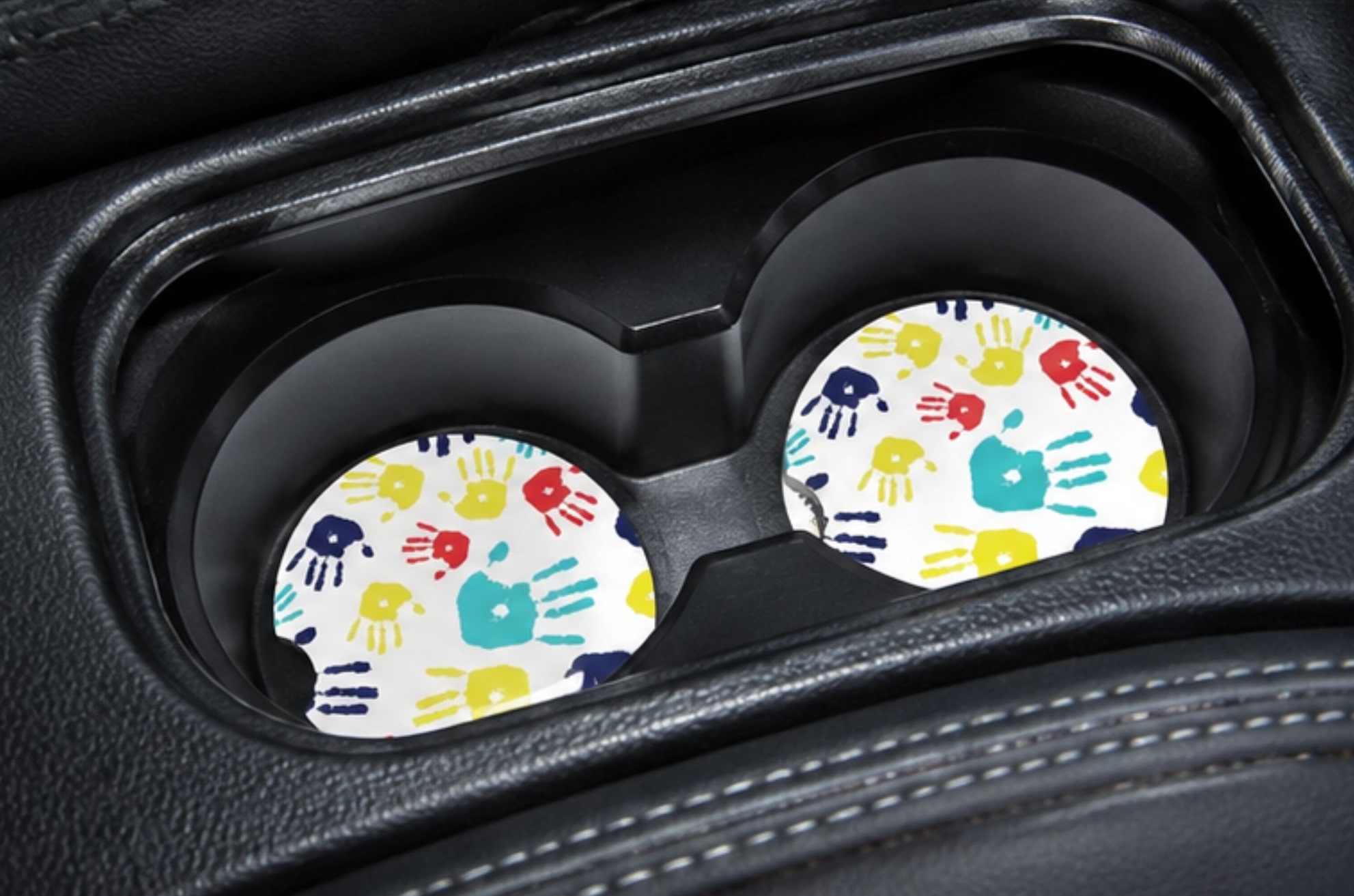 Autism Awareness ceramic car coasters displayed inside vehicle cup holders with colorful kids artwork.