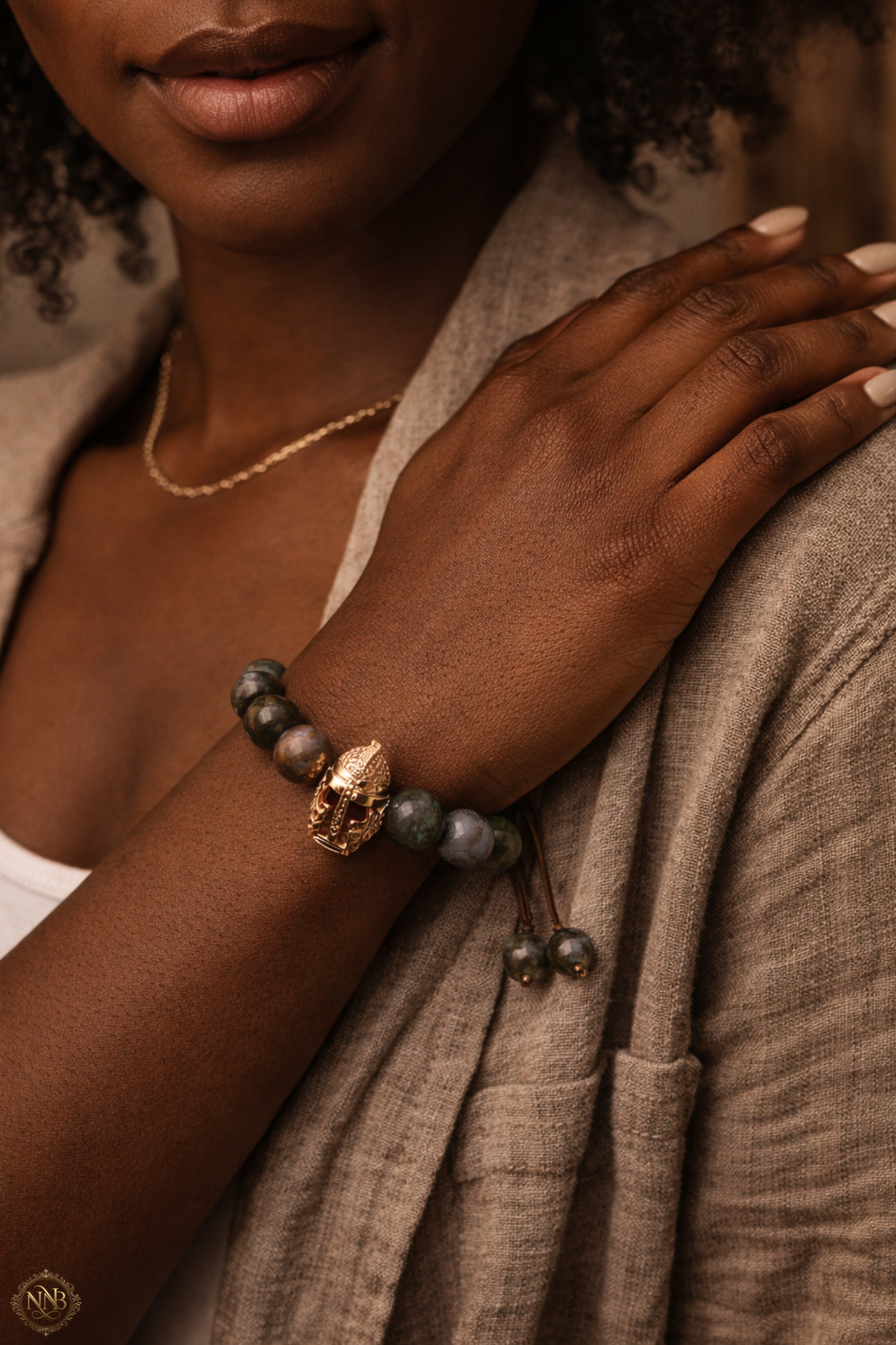 Woman wearing Verdant Vanguard bracelet featuring 12mm natural agate stone beads with rose gold tone Viking helmet centerpiece and adjustable cord, styled in a natural lifestyle setting.