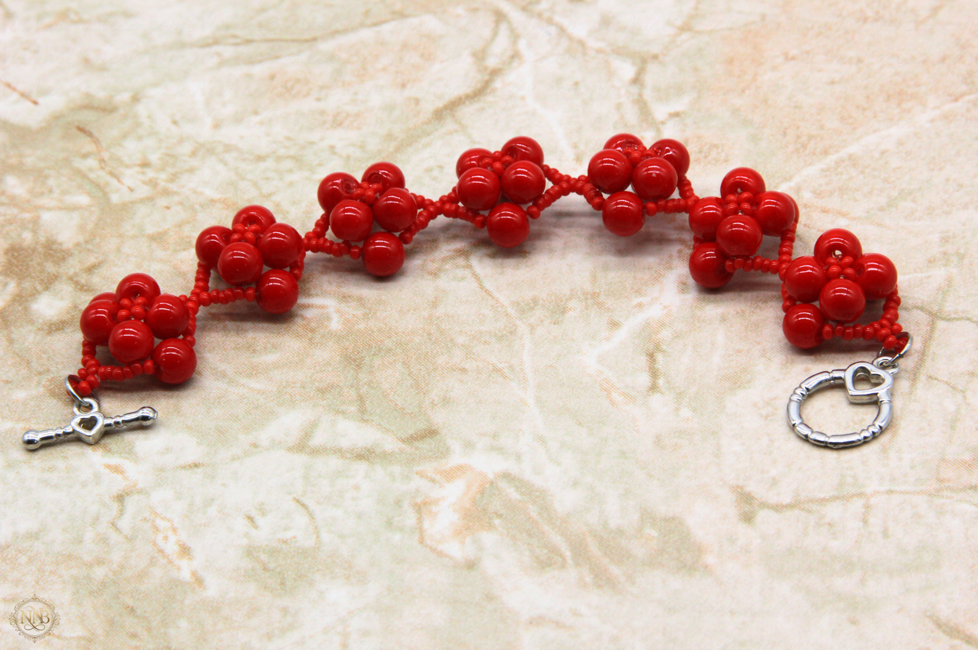 7.5 inch handcrafted red cluster bead bracelet with silver heart toggle closure photographed on neutral marble surface, bold women’s statement jewelry