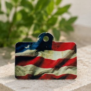 Patriotic sublimation aluminum tag with distressed American flag design displayed on light stone surface with soft greenery background