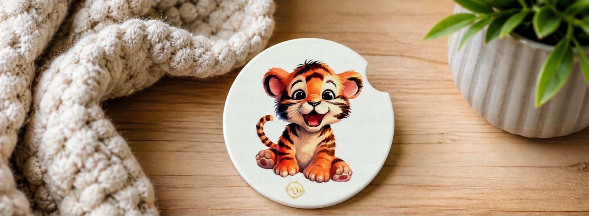 Tiny Tiger ceramic car coaster displayed on a warm wooden surface beside a soft knit blanket and greenery with boutique NicNacBooteek styling.